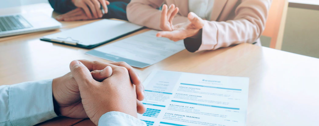 Pessoas com mãos na mesa, pranchetas e papeis na mesa representando laudo de contratação de seguro