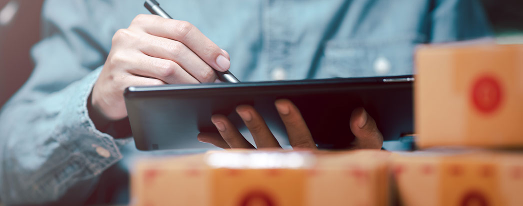 homem com caneta e tablet na mão fazendo inventário patrimonial, caixas a frente