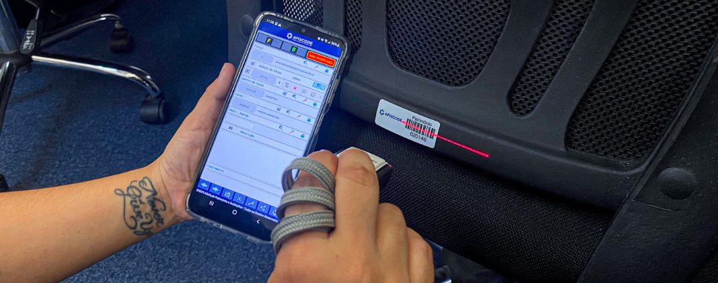 mãos segurando smartphone fazendo inventario atraves do aplicativo afixinv, usando um leitor com a outra mão apontando para qrcode