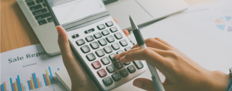 mãos usando calculadra, segurando a caneta, notebook e papeis a mesa