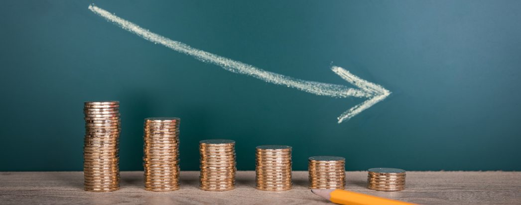 Montes de moedas enfileirados em ordem decrescente com uma seta para baixo simbolizam visualmente a perda de valor ao longo do tempo