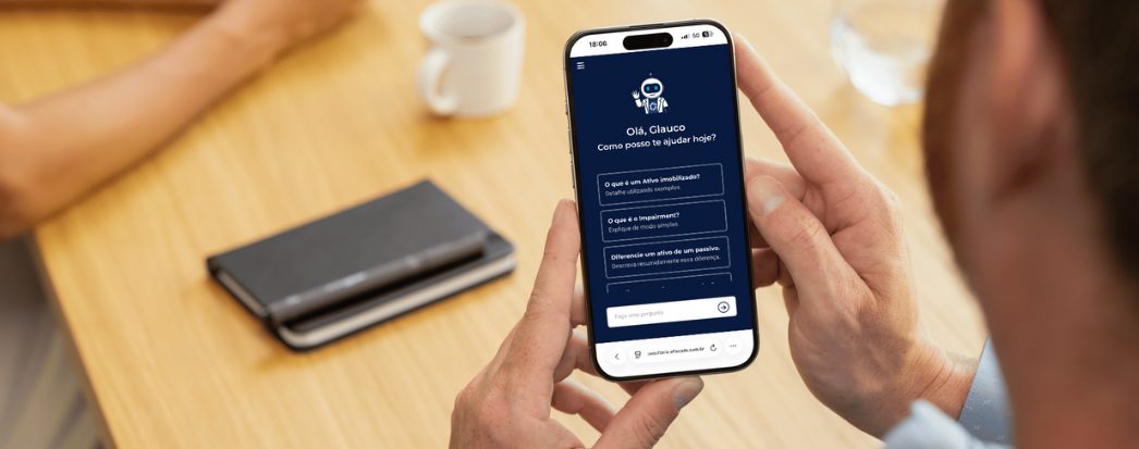 sala de reuniao com braços a mesa, agenda, caneca, angulo de costas, mãos masculinas segurando celular com a tela do consultor ia